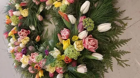 Blomsterkrans med fargerike tulipaner, roser og grønt bar på lys bakgrunn