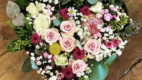 Hjerteformet blomsteroppsats med lyserosa roser og små hvite og burgunder blomster