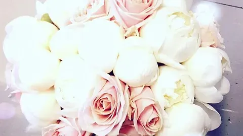 Brudebukett med hvite pioner og lyserosa roser på lys bakgrunn